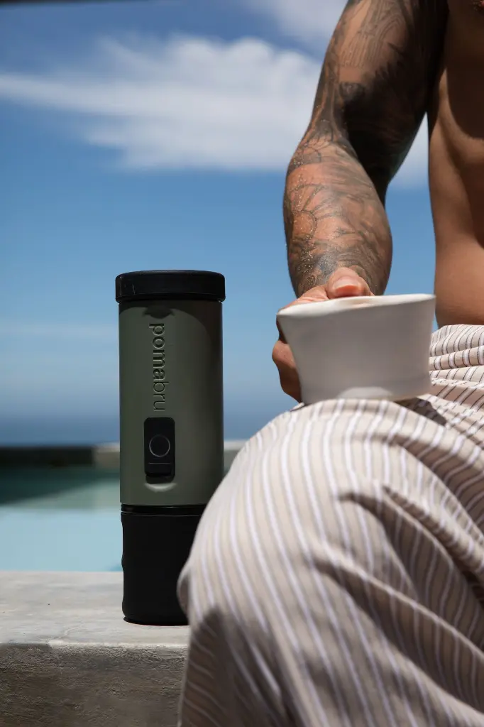 man with coffee cup and pomabru next to pool.webp